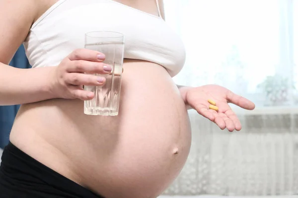 Close-up of a pregnant belly with pills and water in hands, Waiting baby. Pregnancy, expectation of child. Future parens. Prenatal vitamins