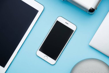 Ofis masaları dizüstü bilgisayar, tablet pc, cep telefonu, hoparlör ve çanta yükü. kopya mavi alanı düz bırakır