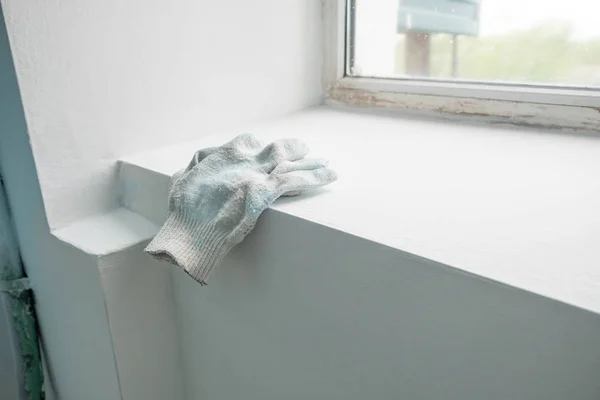 Alçıressamın eldivenleri, inşaat aşamasındaki evin plastik pencereleriyle pencere nin üzerinde yatıyor. Bir apartmanda boyama işleri