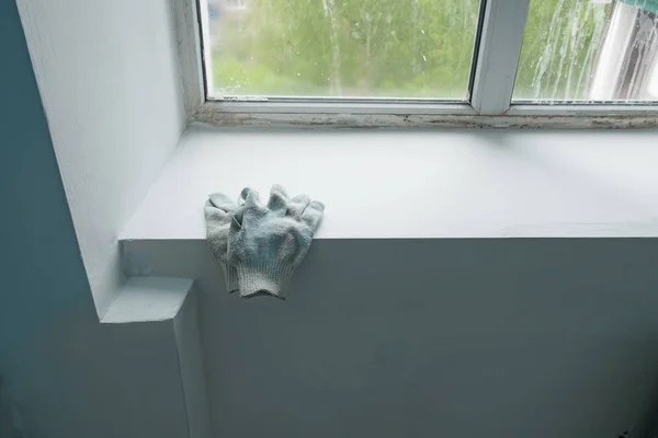 Alçıressamın eldivenleri, inşaat aşamasındaki evin plastik pencereleriyle pencere nin üzerinde yatıyor. Bir apartmanda boyama işleri