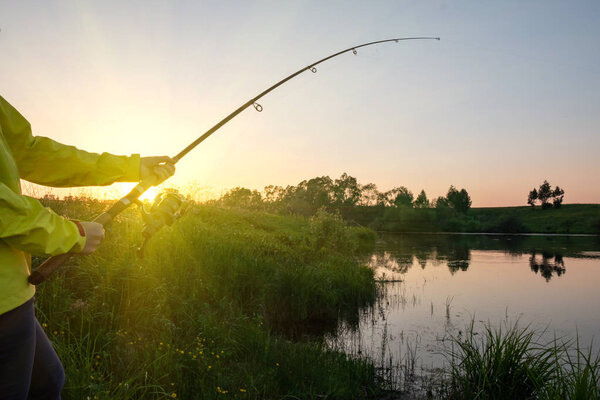 Female hands hold a fishing rod on the lake at sunset. Sunset fishing