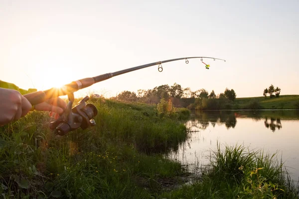 日落时分 女性手在湖上拿着一根钓鱼竿 日落钓鱼 图库图片