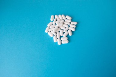 Beyaz ve hap kapsülküçük bir yığın mavi bir arka plan üzerinde yatıyor.