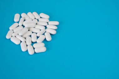 Beyaz ve hap kapsülküçük bir yığın mavi bir arka plan üzerinde yatıyor.