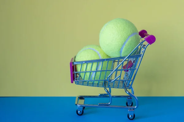 mavi bir yüzey üzerinde bir gıda arabası sepeti iki tenis topları. spor malzemeleri satışı