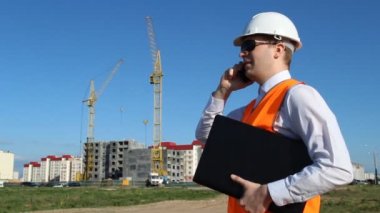 siyah gözlük denetçisinde bir dizüstü bilgisayar tutarak ve konut bir ev inşaatı zemin üzerine telefonda konuşuyor