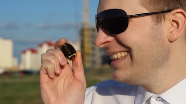 Um homem de óculos pretos segura um etério na mão e sorri maliciosamente, se alegra — Vídeo de Stock