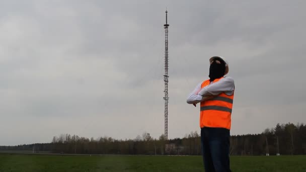 Człowiek w czarna maska i kurtka alarmu jest stojący w pobliżu wieży radiowej, Szpieg — Wideo stockowe