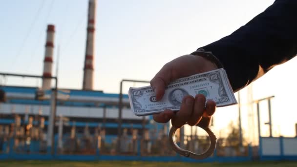 Рука человека в пиджаке держит деньги в наручниках на фоне электростанции, закате, крупном плане — стоковое видео