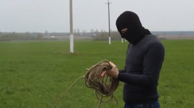 Bir ip ile siyah maskeli bir adam yüksek gerilim kabloları çalmaya çalışır