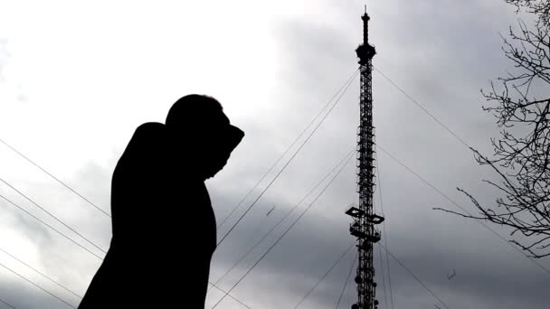 A man emotionally talks on the phone against the background of a telephone tower, waves his hands — Stock Video