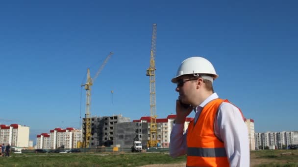 Старшина разговаривает по телефону на фоне строительства жилого дома — стоковое видео