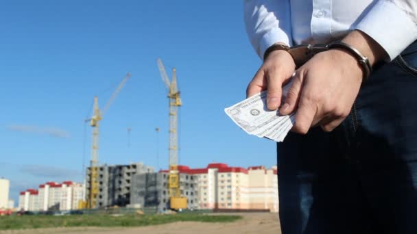Ο αρχηγός σε ένα λευκό πουκάμισο με χρήματα δολάρια είναι δεμένος με χειροπέδες με φόντο η οικοδόμηση ενός σπιτιού, γκρο πλαν — Αρχείο Βίντεο