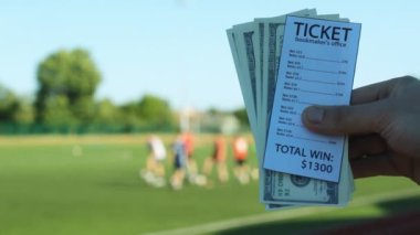 Bir adam elinde bir bilet bahis ofisi ve para dolar nerede futbol, spor bahisleri oynamak stadyumun arka planı tutuyor