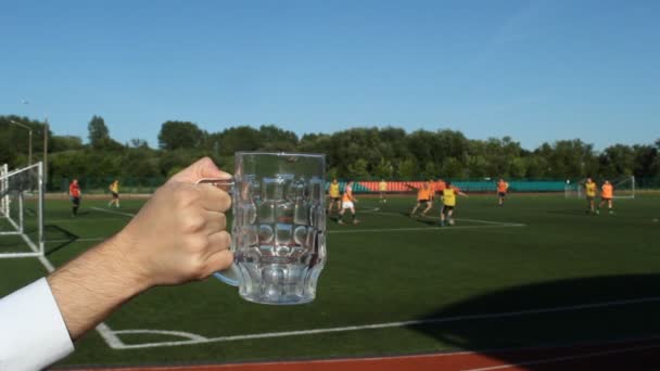 Un hombre vierte cerveza en un vaso contra el telón de fondo del estadio de fútbol — Vídeo de stock