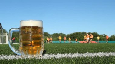 Bir bardak bira standları bir futbol sahası üzerinde yeşil çimenlerin üzerinde oyuncular futbol oynamak.