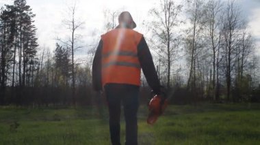Bir adam bir chainsaw ve sinyal yelek ormana gelir