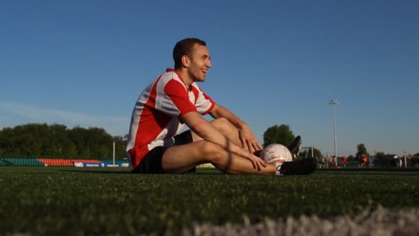 Jugador está sentado en la hierba y sonriendo — Vídeos de Stock