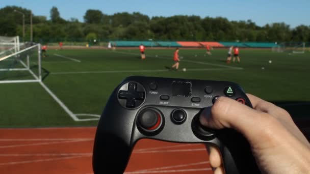 Mens händer hålla en spelet joystick och tryckknappar på bakgrunden av arenan där de spelar fotboll — Stockvideo