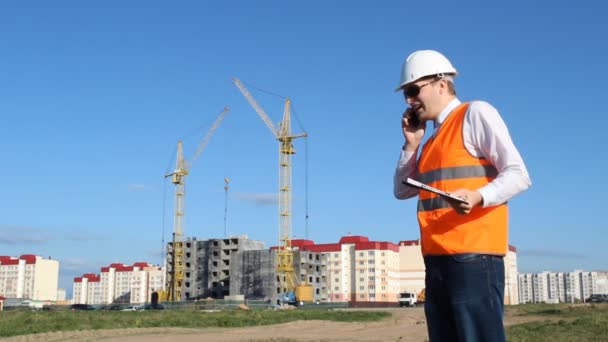 Un jefe malvado un inspector con una tableta hablando por teléfono, dando órdenes, regañando, en el contexto de la construcción — Vídeo de stock