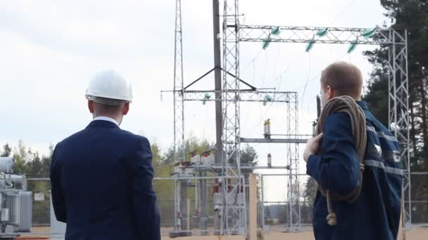 Der Chef übergibt dem Arbeiter vor dem Hintergrund des Kraftwerks die Befehle — Stockvideo