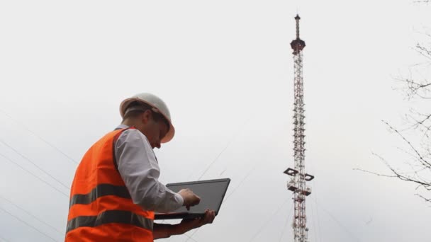 Een man-inspecteur gegevens invoert in de laptop en kijkt naar de telefoon toren — Stockvideo