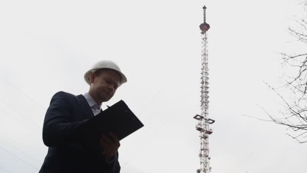 Inspector trabalhador registra informações sobre a torre de telefone na pasta e olha para ele — Vídeo de Stock