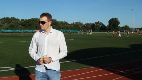 Man in handboeien met geld dollars in de handen, op een achtergrond van voetbalveld, spelers voetballen — Stockvideo