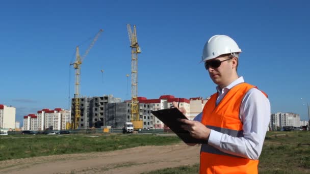 El inspector de gafas negras realiza una inspección de la construcción de una casa residencial, marca una tableta — Vídeo de stock