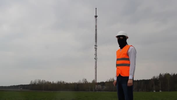 Een man in een zwart masker, een spion, wrijft zijn handen tegen de achtergrond van een radiotoren, toren van de telefoon, interceptie van informatie — Stockvideo