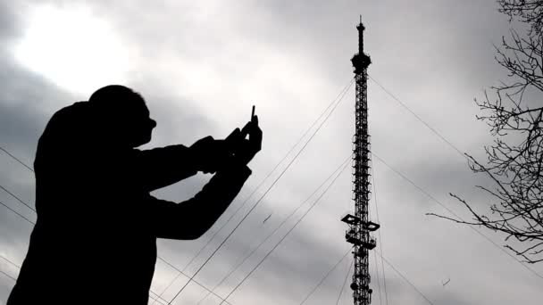 Человек с двумя телефонами ищет доступную сеть на фоне телефонной вышки, плохой сигнал — стоковое видео