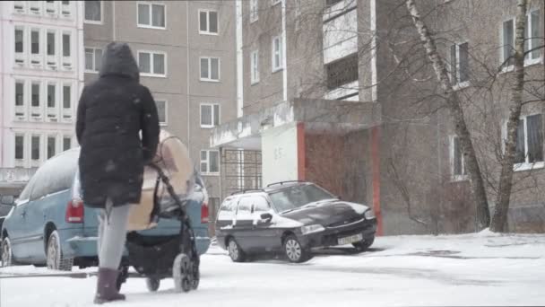 Une mère avec un enfant dans une poussette marche dans une forte chute de neige — Video