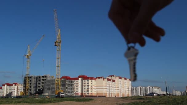 La main des hommes tient les clés de l'appartement sur le fond de la construction d'une maison d'habitation, un gros plan — Video