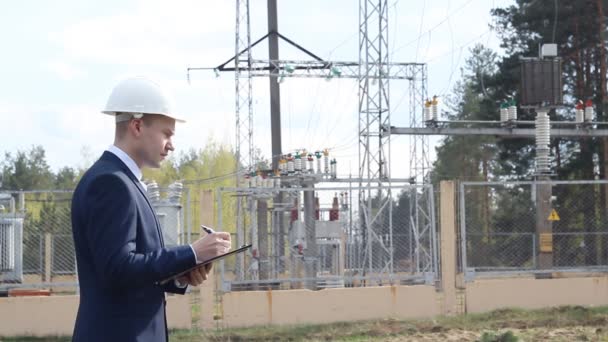 Un joven ingeniero en el fondo de una central eléctrica escribe datos en una tableta — Vídeos de Stock