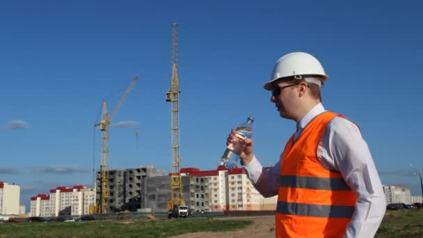 Chefen skall inspektören dricker vatten på bakgrunden av bygga hus — Stockvideo