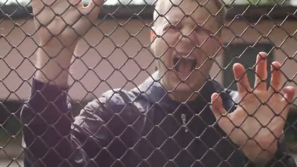 Nerveus criminele gevangene schreeuwt en slaat zijn handen op het raster, toont agressie, opsluiting, gevangenis en een oneerlijke zin, slow-mo — Stockvideo
