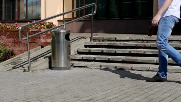 En ung man kastar en plastflaska i staden, nära en papperskorgen kan, en förbipasserande går och plockar upp skräp efter honom och kastar den i papperskorgen — Stockvideo