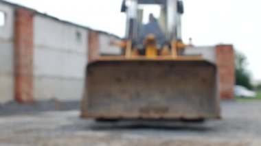 Büyük bir kova ile büyük bir sarı yükleyici doğrudan kameraya, bulanık, büyük kepçe sürmek.
