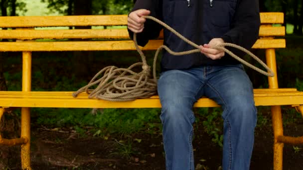 Un uomo si siede su una panchina e fa un cappio dalla corda, si prepara al suicidio, si prepara al suicidio, si impicca — Video Stock