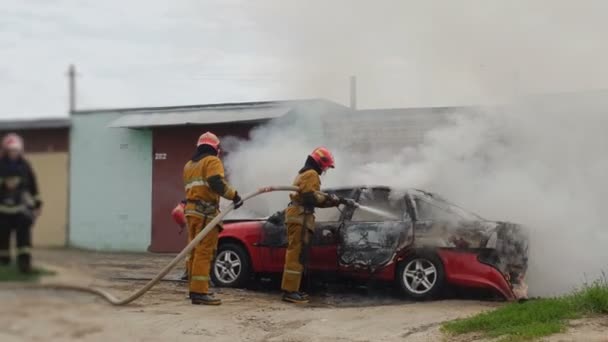 Пожарные или пожарные тушат горящую машину после террористического акта — стоковое видео