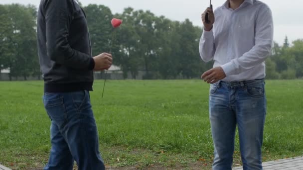 Ein Mann schenkt einem anderen ein rosafarbenes Herz, Homosexualität, gleichgeschlechtliche Ehe, Regen, Zeitlupe — Stockvideo