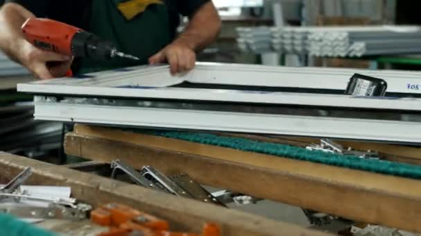 Produktion und Herstellung von PVC-Fenstern, ein männlicher Arbeiter montiert ein PVC-Profilfenster, bohrt ein Loch in das PVC-Profil für die Montage von Scharnierteilen, bohrt — Stockvideo