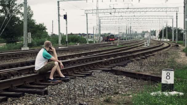 Homme est assis sur le chemin de fer ou chemin de fer et parlerIng sur le smartphone, la vie en danger — Video
