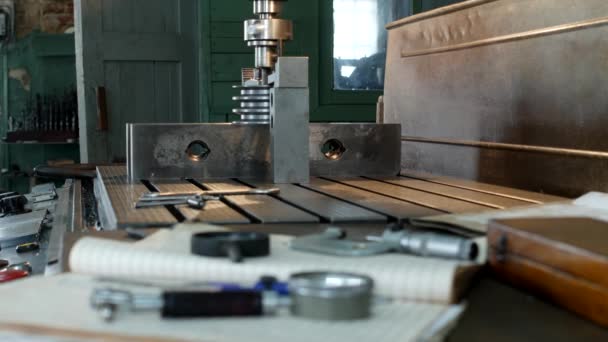 Un taller privado para trabajar con piezas metálicas, en el fondo una máquina de perforación perfora un agujero en la polea, en la mesa se encuentran los instrumentos de medición, la medición — Vídeos de Stock