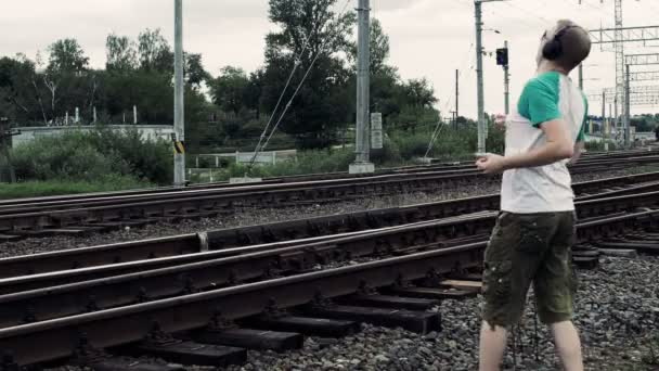 Man listening to music on earphones and inattentively crosses a railway or railroad, life threatening — Stock Video