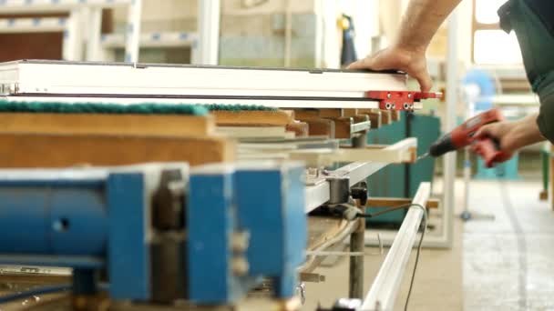 Produktion och tillverkning av pvc-fönster, en manlig arbetstagare monterar ett pvc profil fönster, borrar ett hål i pvc profil för montering gångjärn delar, pvc ram — Stockvideo