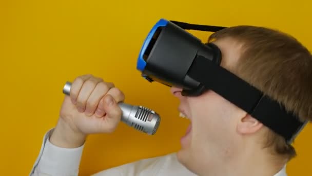 Homem com fone de ouvido realidade virtual e microfone canta, no fundo da parede amarela — Vídeo de Stock