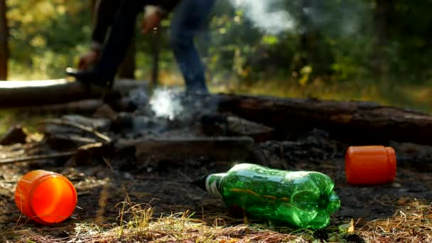 Em primeiro plano em uma clareira florestal há garrafas de plástico de lixo, incêndios estão fumando, as pessoas andam no fundo, recreação ao ar livre, poluição pelo lixo — Vídeo de Stock