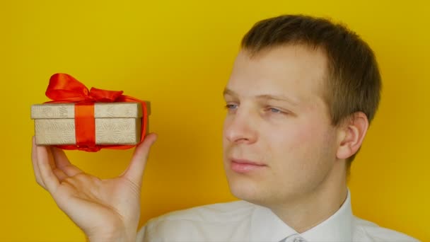Хлопець з подарунком всередині коробки посміхається і дивиться в камеру, на жовтому фоні стіни — стокове відео
