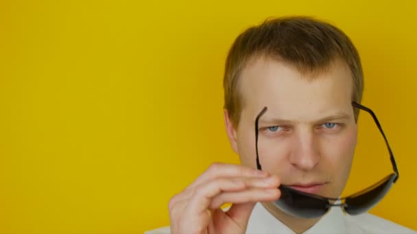 Portrait of serious man in white shirt with black glasses, on yellow wall background — Stock Video